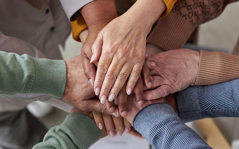 A group of older adults touching hands in a circle.