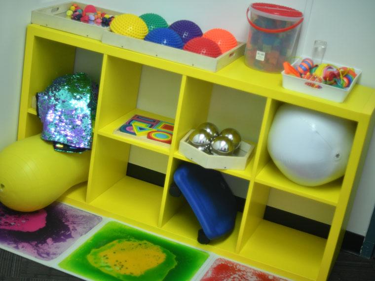 Yellow shelving with brightly coloured items on display in the Multi-Sensory Room.