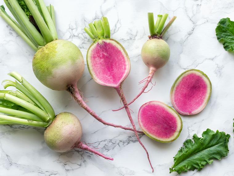 Top view of watermelon radishes and green leaves on a countertop. 