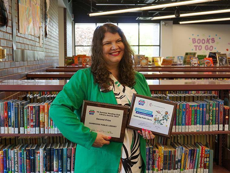 Andrea Siemens holds two award plaques in front of book shelves in the Queen's Square Children's Department