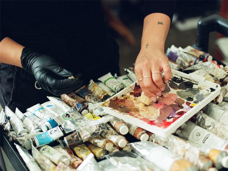 A photograph of hands mixing a oil paints. Several tubes of oil pain rest nearby.