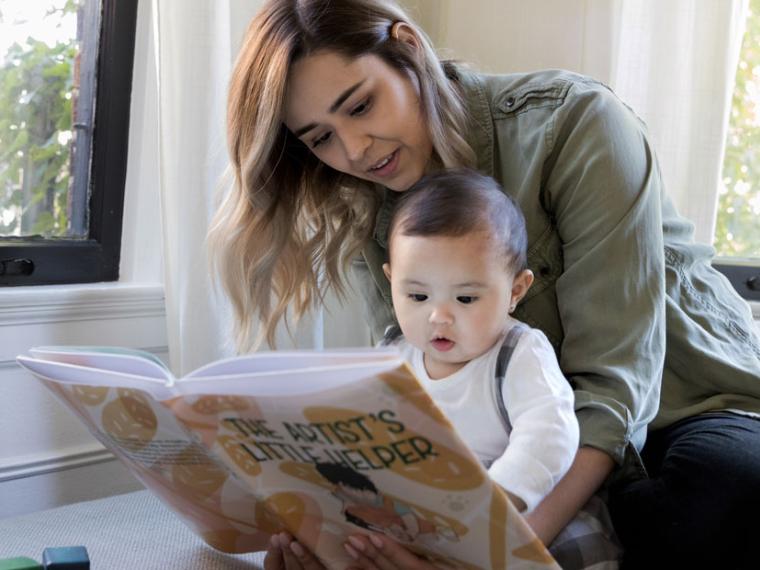 Adult and baby reading an open book on a sofa.