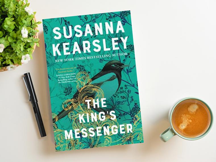 A copy of The King’s Messenger on a table with mug, plant, and pen next to it.