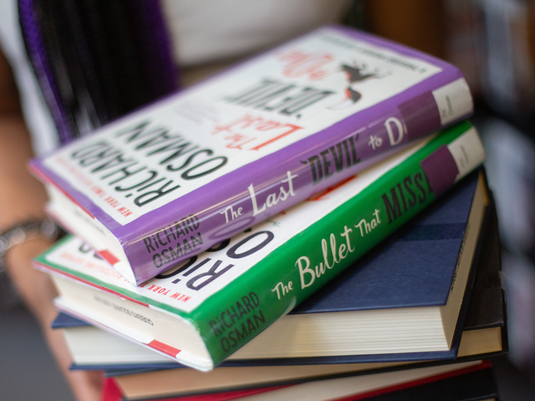 A person holds a stack of books including two by Richard Osman.