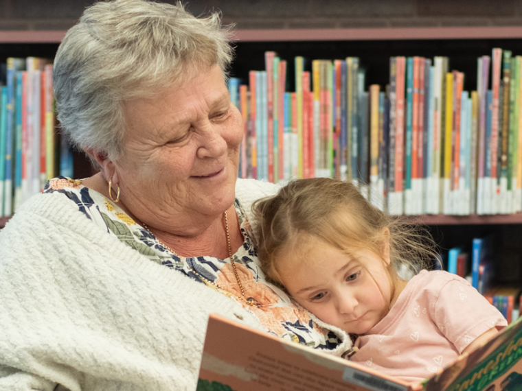 Grandparent and child reading a book together in the library.