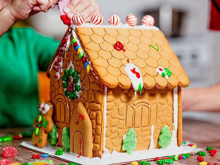 Person adding icing to a gingerbread house decorated with candy.