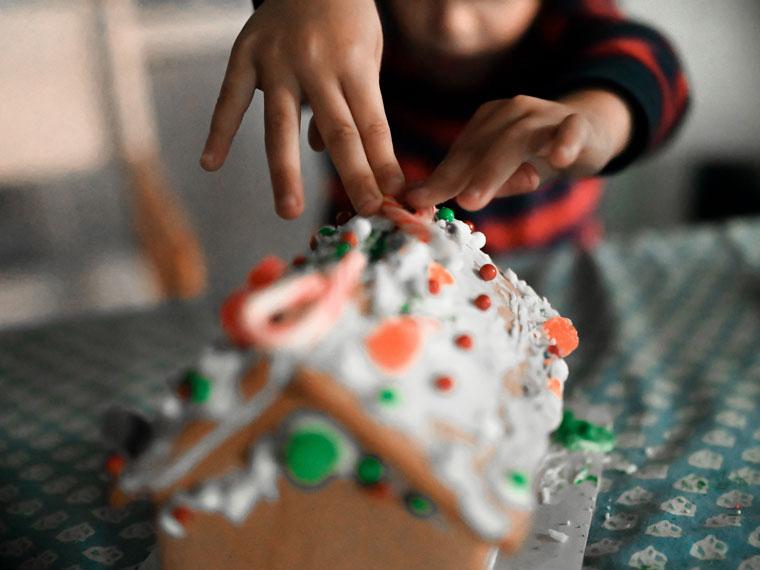 Child decorating homemade gingerbread house with candy.