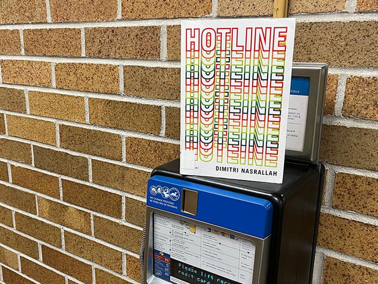 Copy of Hotline book sitting on the top of a payphone on a brick wall.