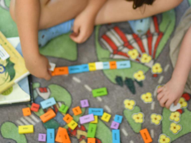 Two children playing with a Read the Rainbow kit on a colourful rug.