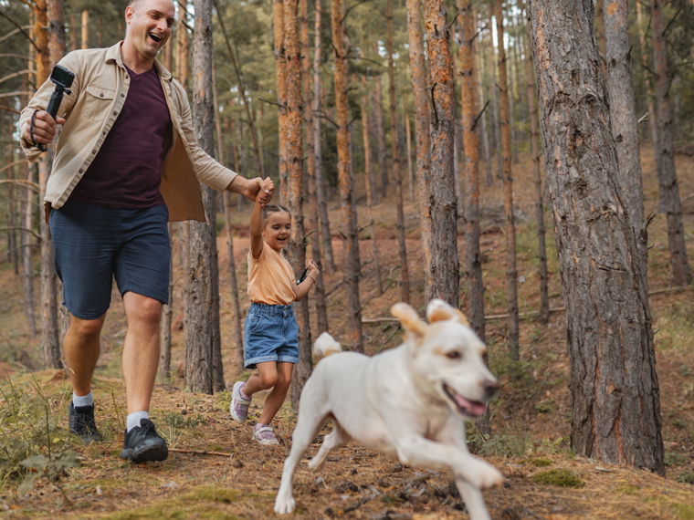 A man and his young daughter walking a white dog on a hiking trail