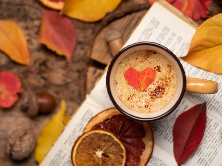 Cup of coffee and autumn leaves sitting on an open book.