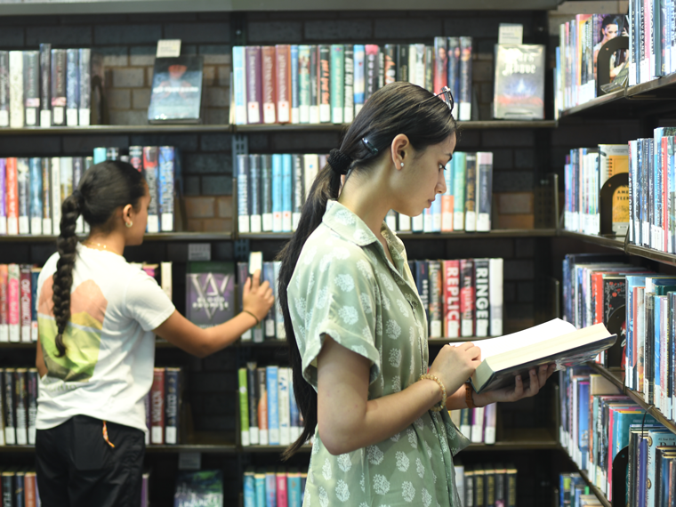 Two students in front of a book shelf selecting books.