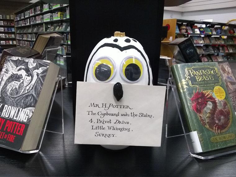 A pumpkin decorated as Hedwig from the Harry Potter books on a shelf with books. 