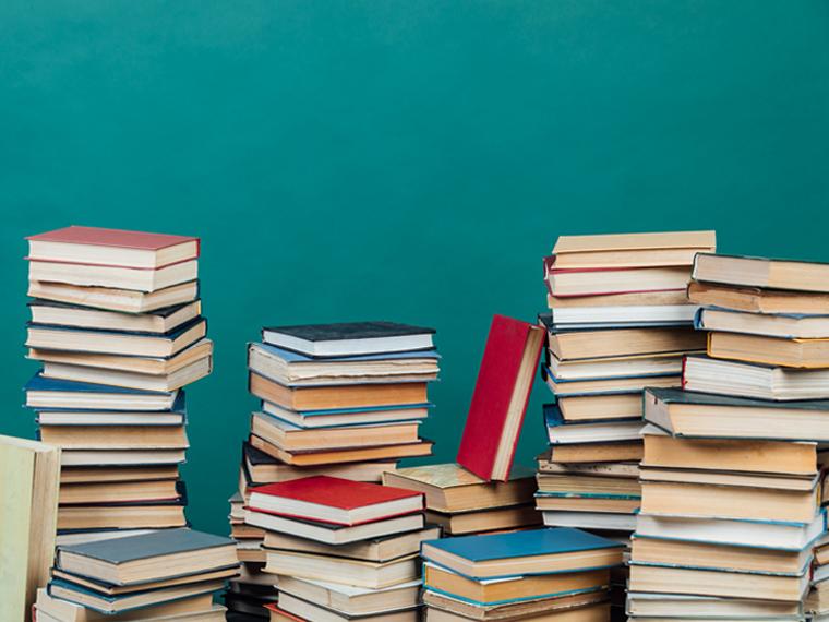 Stacks of books on a table in front of a teal wall