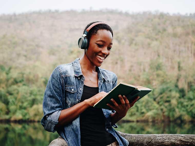 Woman wearing headphones, reading a book, smiling