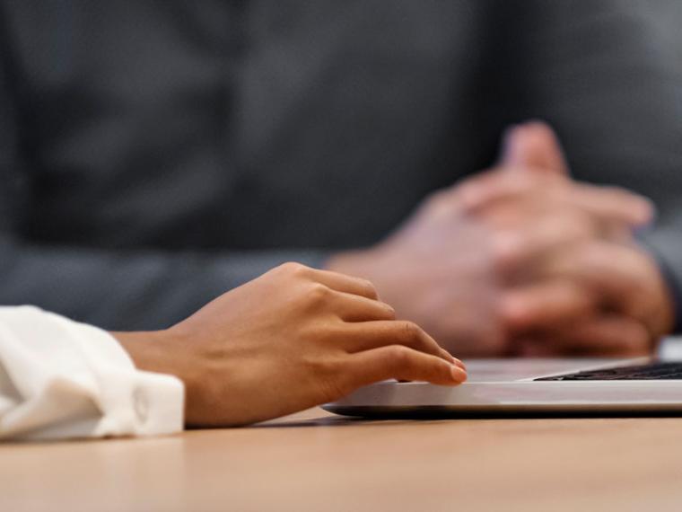 Close-up of hands working at a desk with a laptop.
