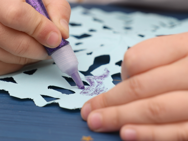 Close-up of a child making snowflake craft at a wooden table.