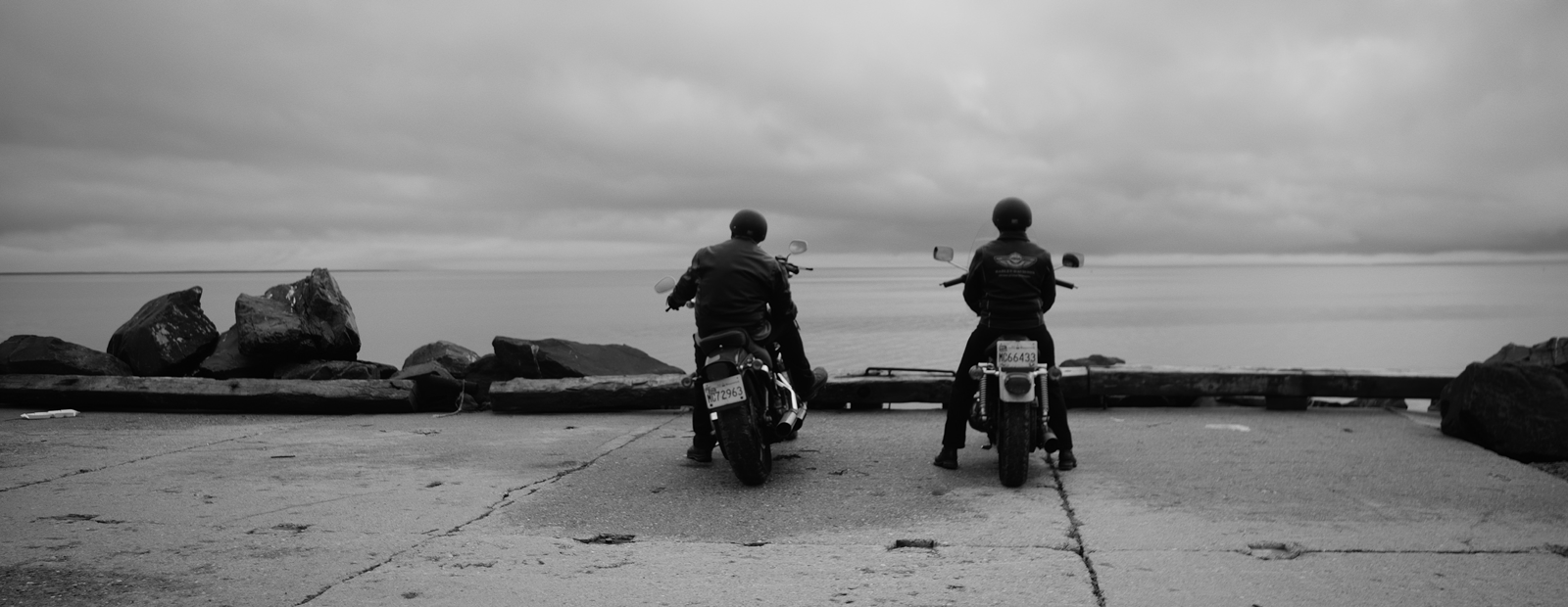 Two adults sitting on parked motorcycles overlooking an ocean.