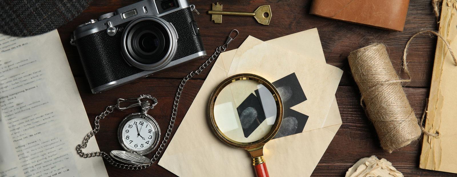 Vintage items on wooden background including a camera, pocket watch, and magnifying glass.