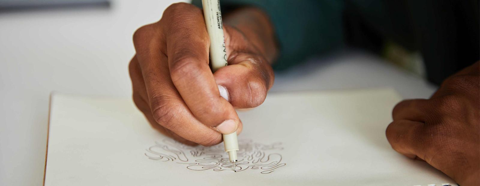 A photograph of hands drawing in a sketchbook