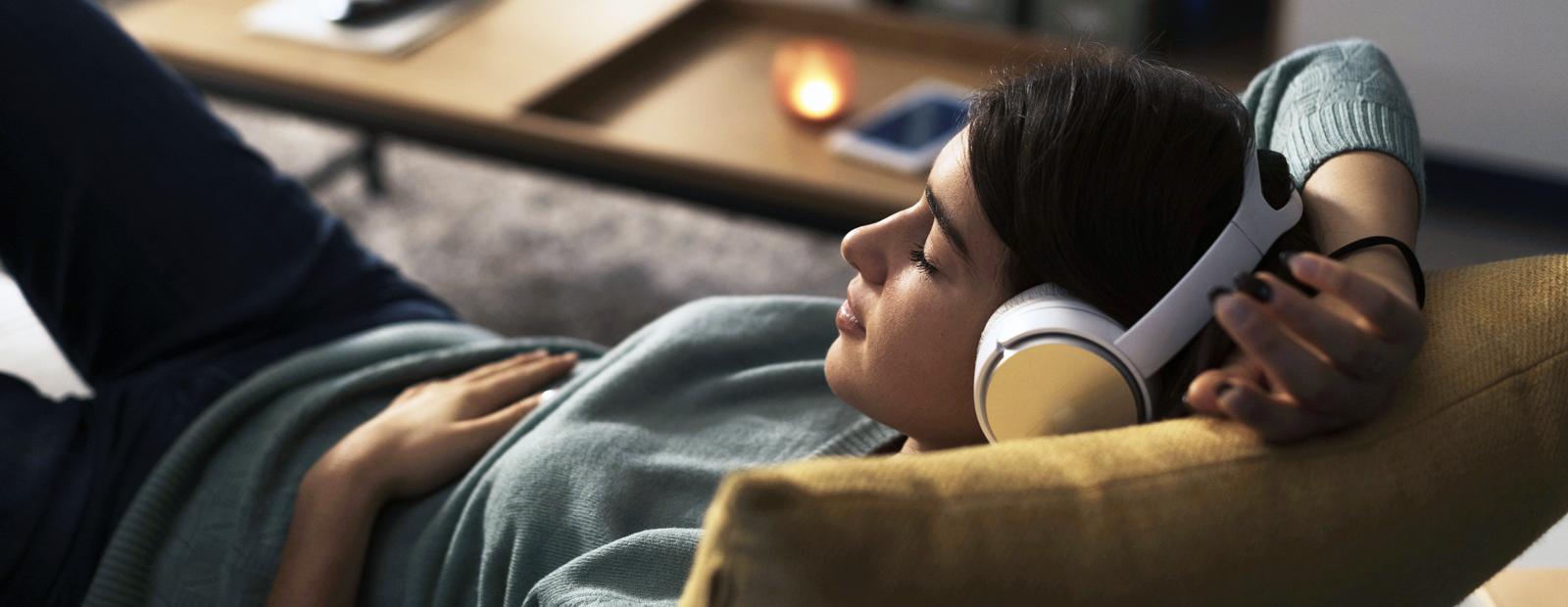 Person resting on the couch at home wearing wireless headphones and listening to music.