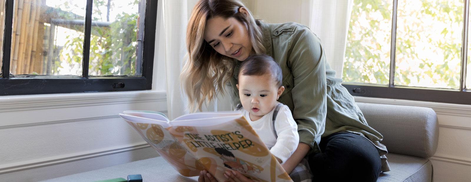 Adult and baby reading an open book on a sofa.