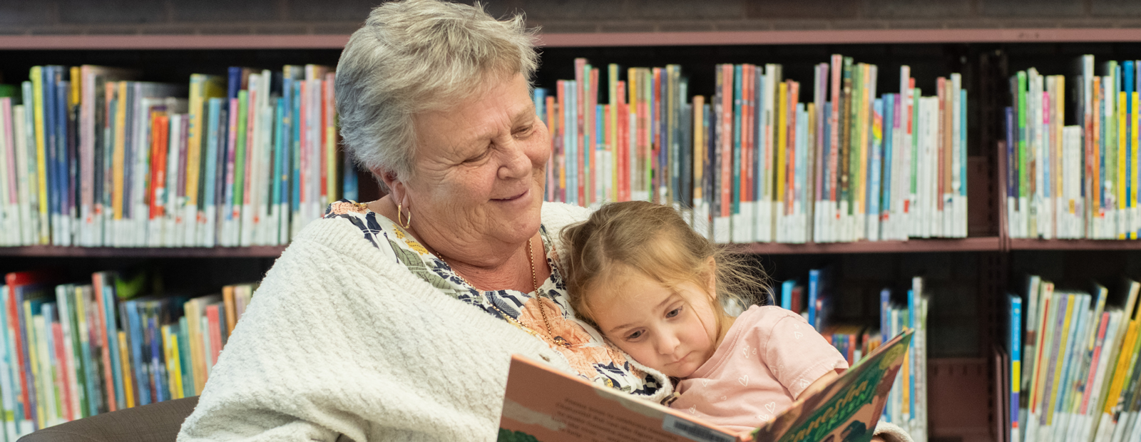 Grandparent and child reading a book together in the library.