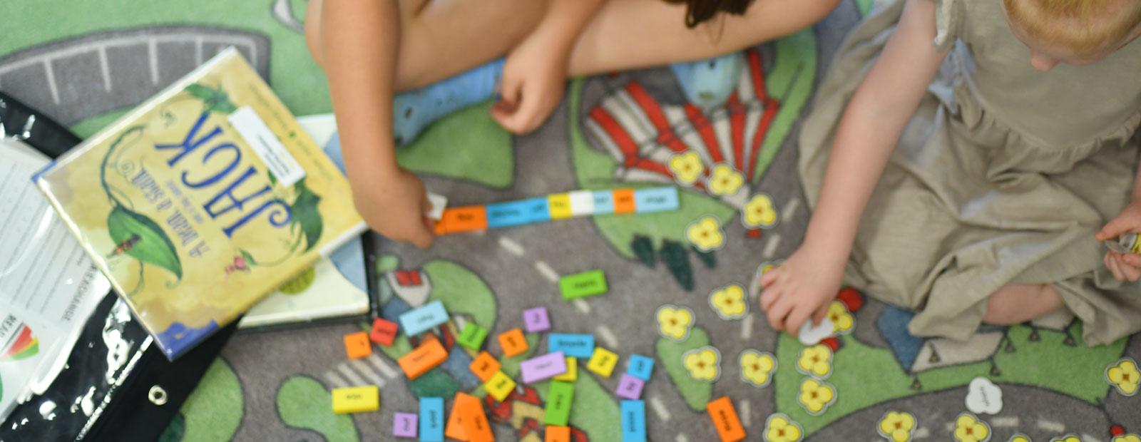 Two children playing with a Read the Rainbow kit on a colourful rug.