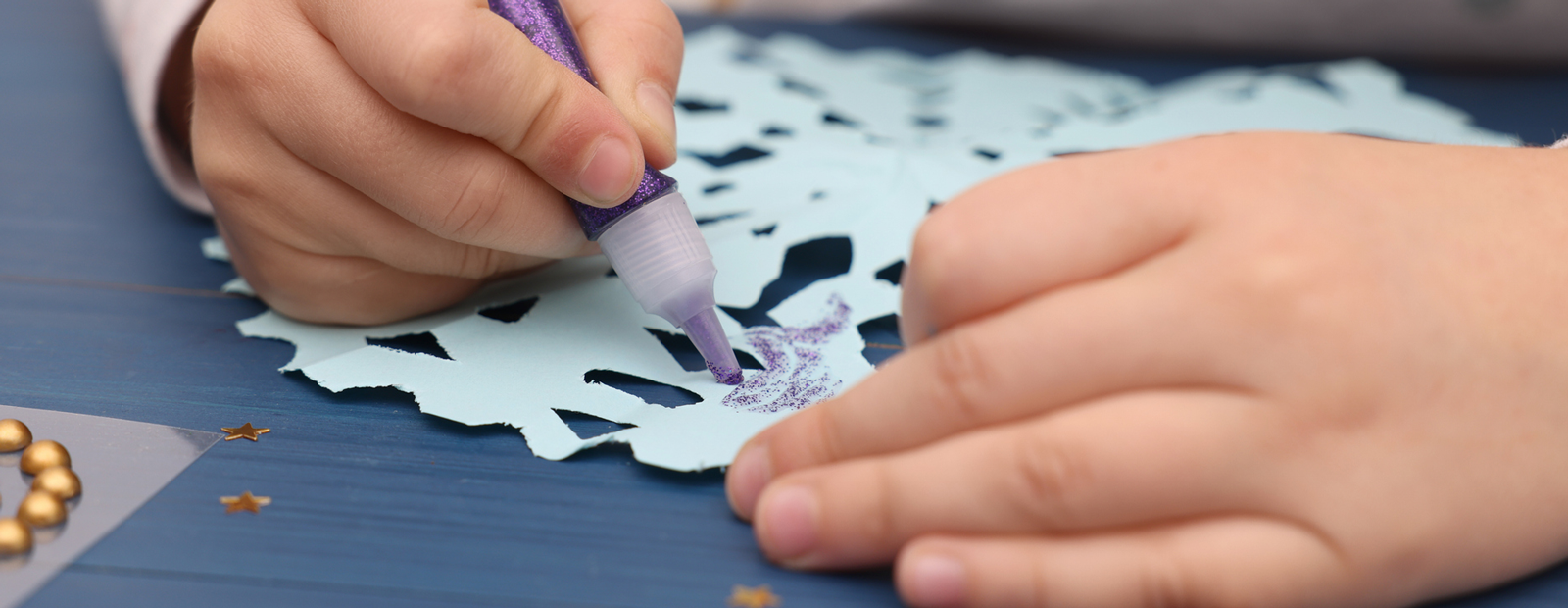 Close-up of a child making snowflake craft at a wooden table.