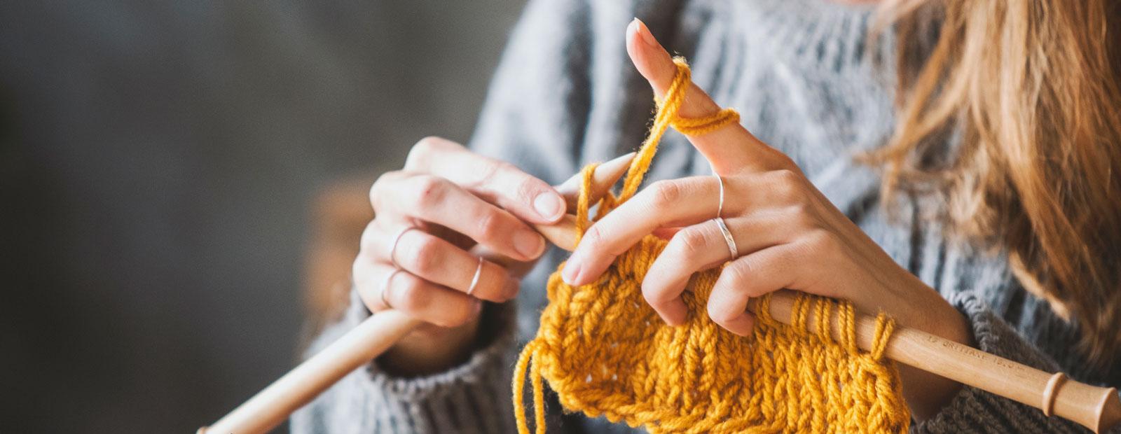 Close up on woman's hands knitting with yellow yarn