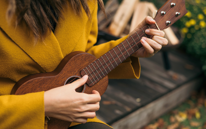 A close-up of an adult playing a ukulele outside on a terrace.