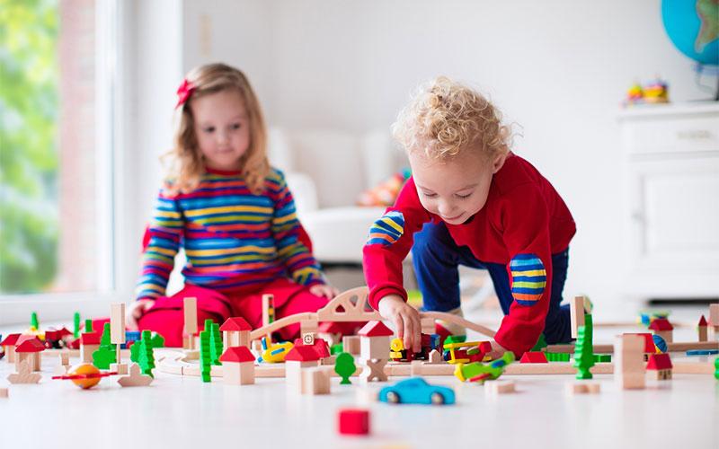 Two children playing on the floor with wooden blocks and cars.