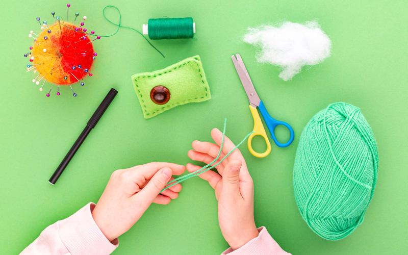 Hands holding thread on table with other crafting and sewing materials.